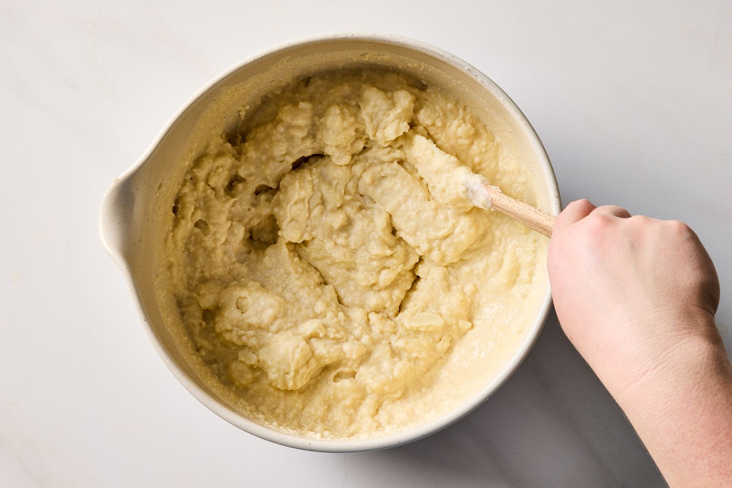 A bowl of mashed potatoes being stirred by hand with a spoon