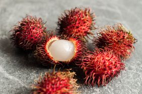rambutan fruits, one opened on grey surface