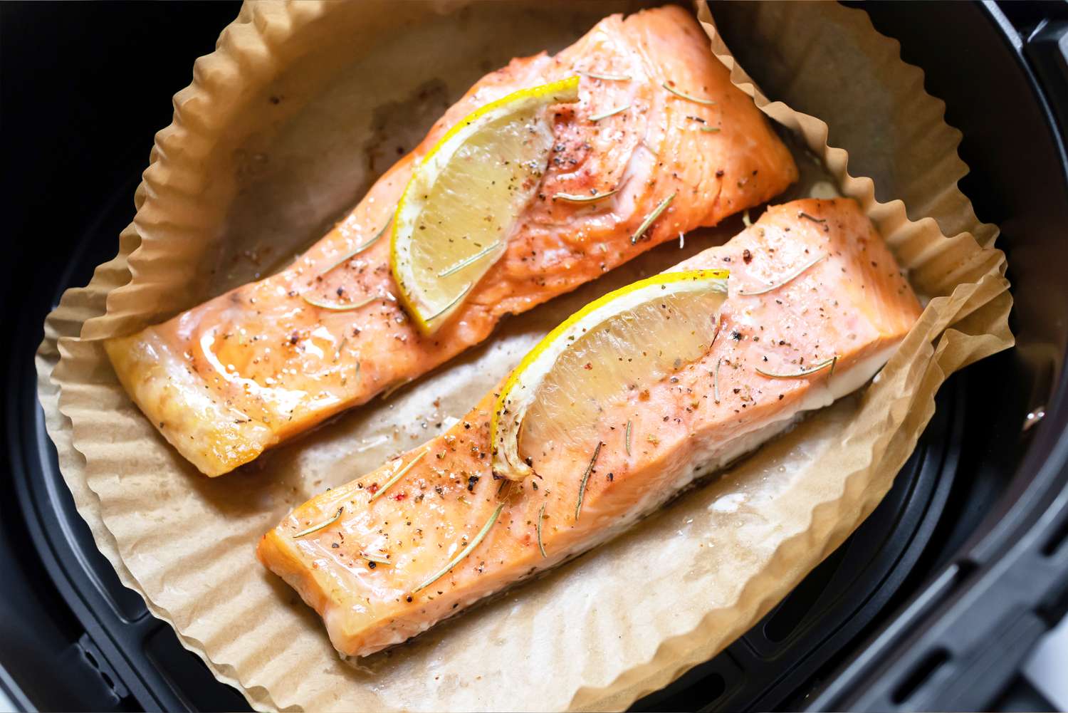 Salmon fillets in an air fryer garnished with lemon slices