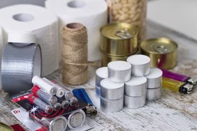 Emergency preparedness supplies including candles, batteries, canned food, and toiletries on a table