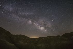A starry sky with the Milky Way galaxy visible over dark hilly terrain