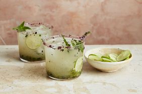 Two glasses of a lime-based beverage beside a bowl of lime slices