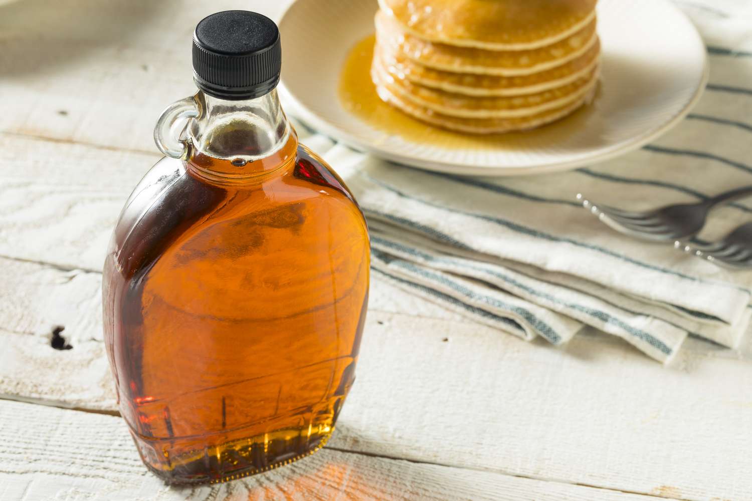 A bottle of syrup on a table with pancakes in the background