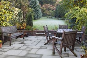 Outdoor patio with wooden furniture overlooking a wellmaintained green backyard with various trees and plants