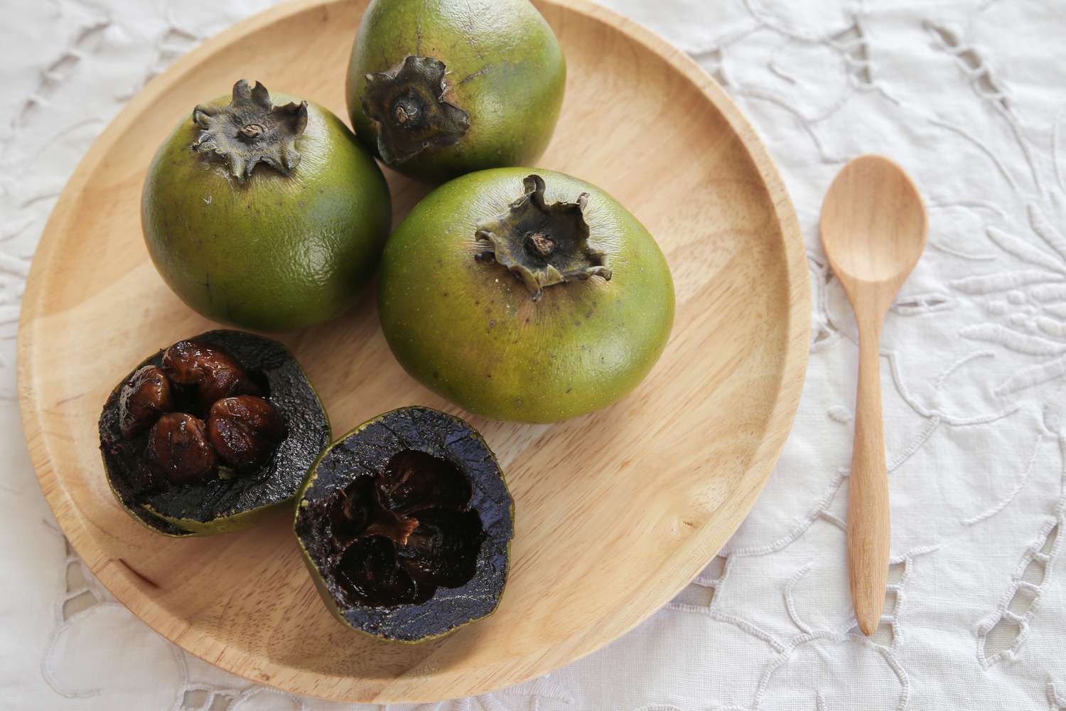 Black sapote with green skin and black fruit cut open on a plate