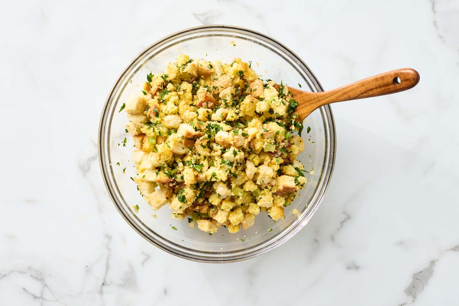 Bacon and cornbread stuffing in a glass bowl with a wooden spoon