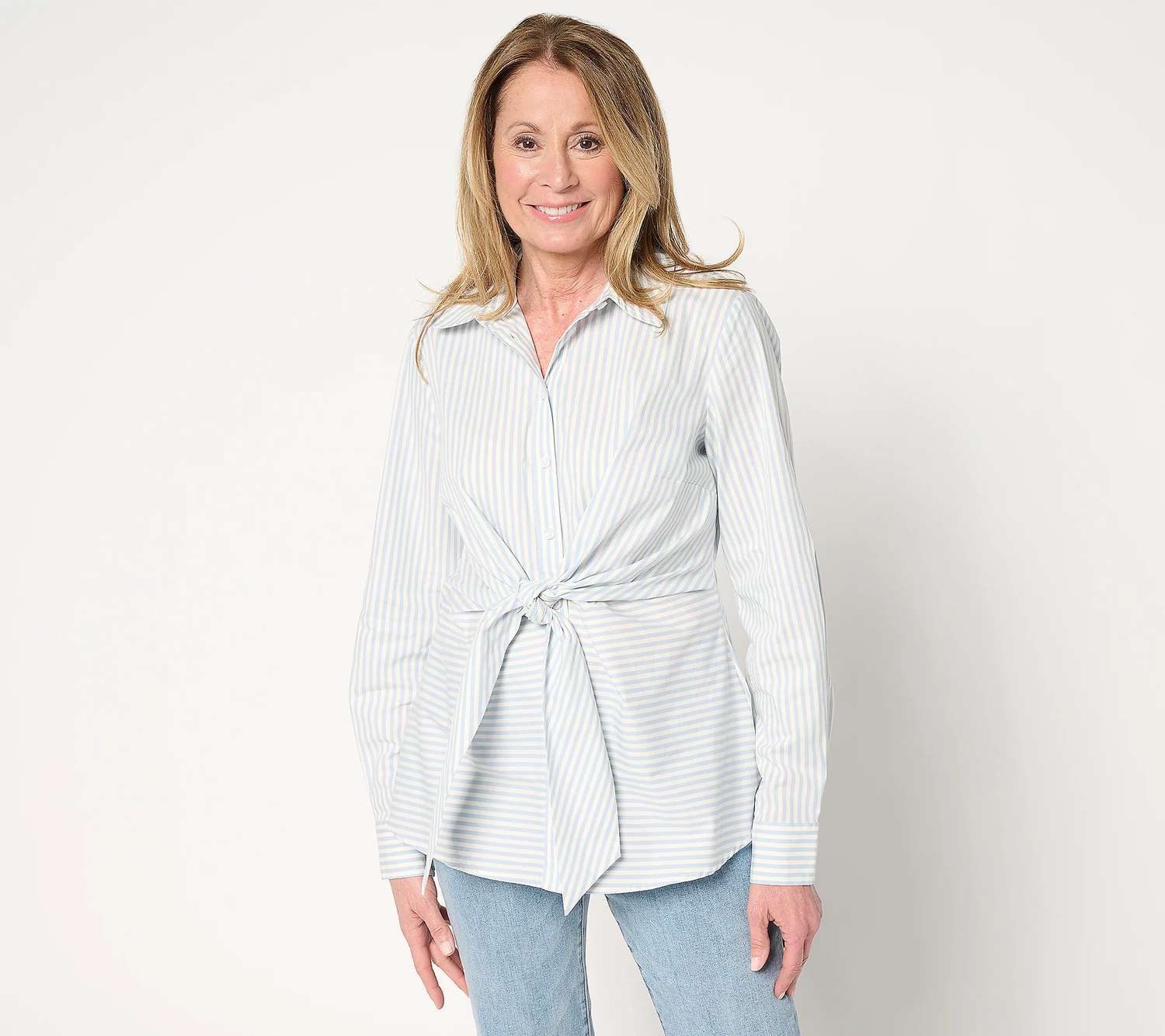 Person wearing a striped shirt with a front tie detail and jeans standing and smiling. 