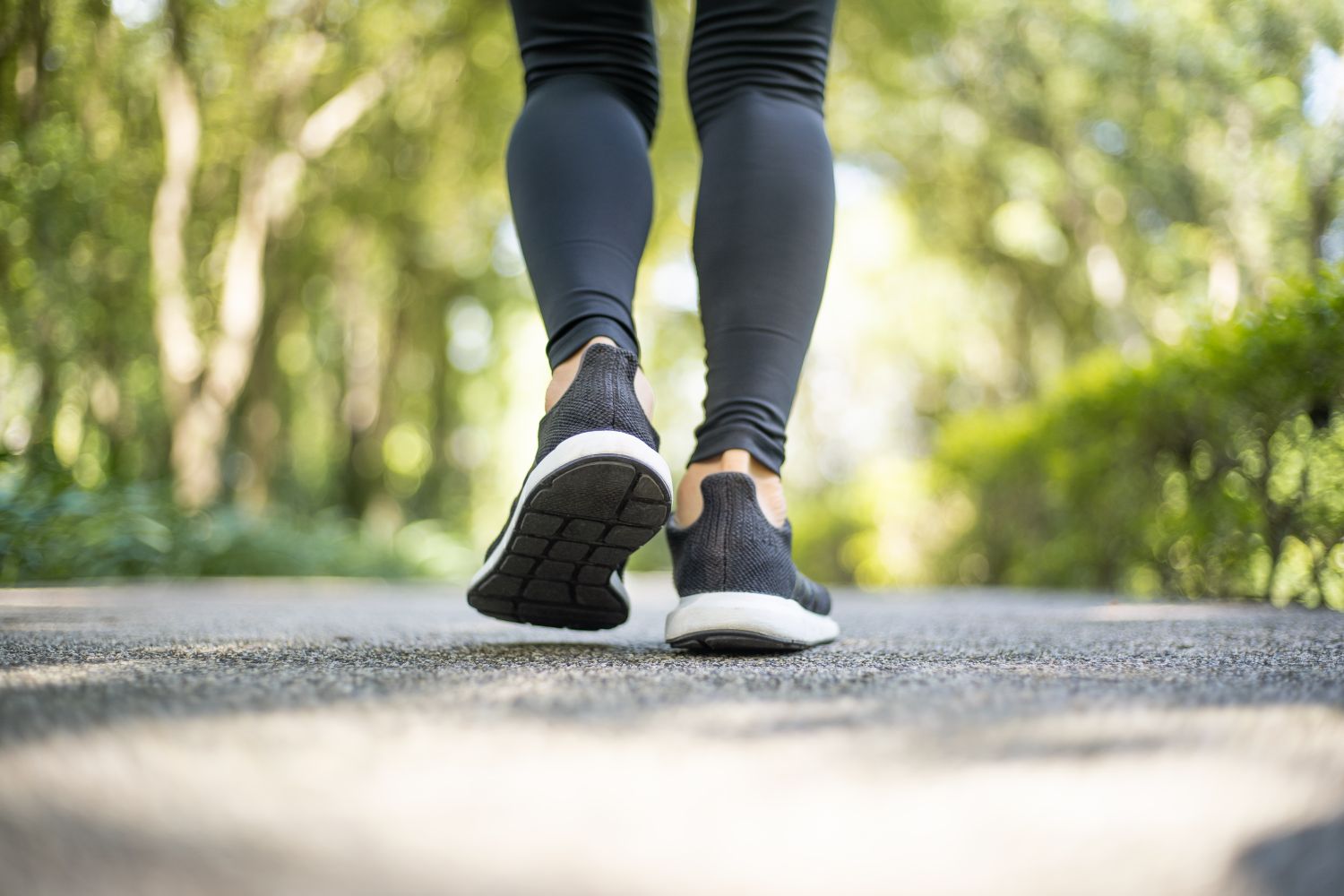 Person walking outdoors on a paved path surrounded by greenery
