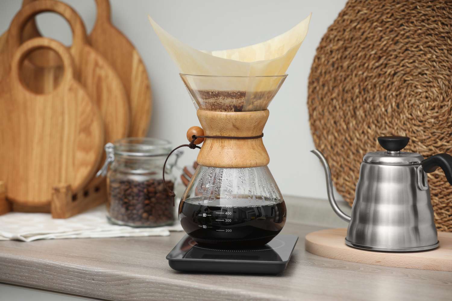 Making drip coffee. Glass chemex coffeemaker with paper filter, jar of beans and kettle on wooden countertop in kitchen