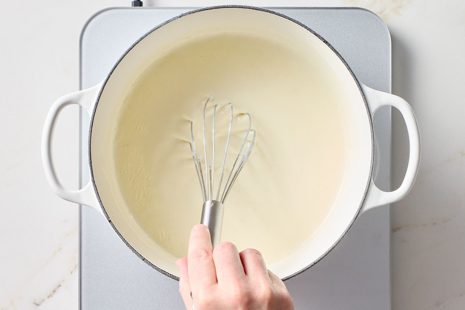 Whisk stirring a creamy sauce in a white pot on a stovetop