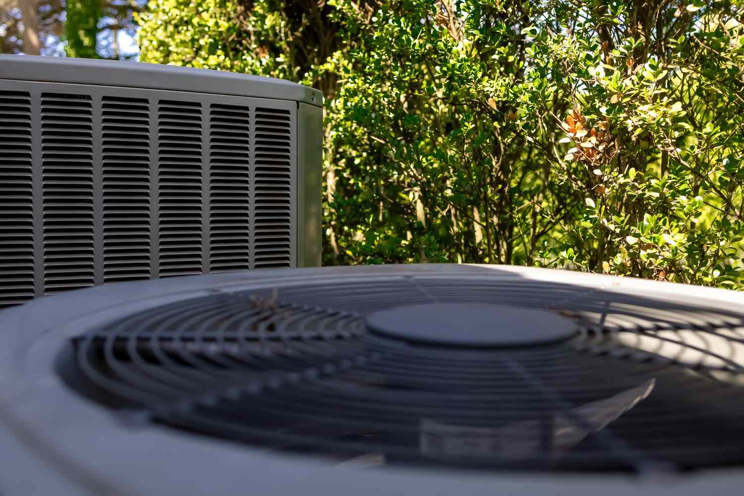 An outdoor air conditioning unit with a fan in the foreground, surrounded by greenery