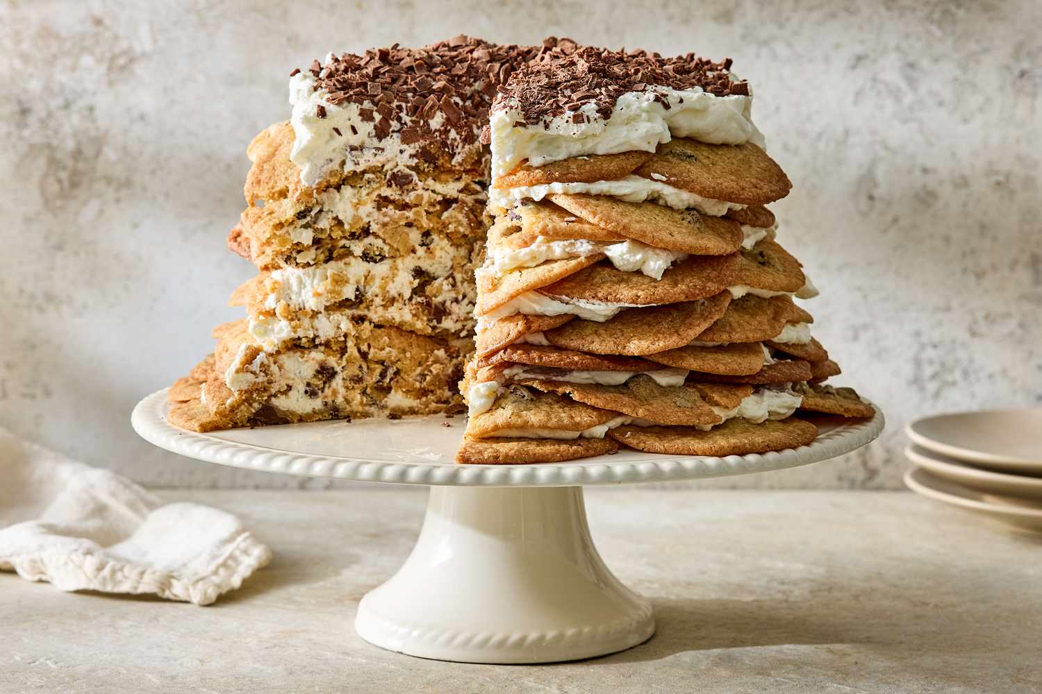A layered chocolate chip cookie icebox cake on a ceramic stand with a slice taken out to show the layers