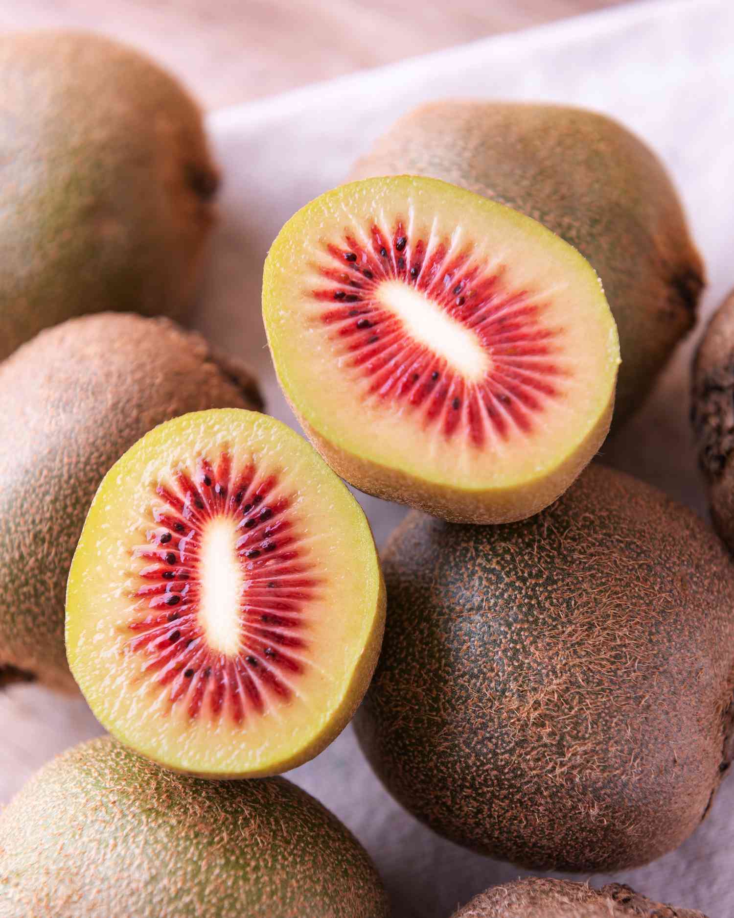 red kiwi sliced in half resting on whole kiwis