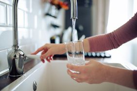 A person filling a glass with water from a kitchen faucet