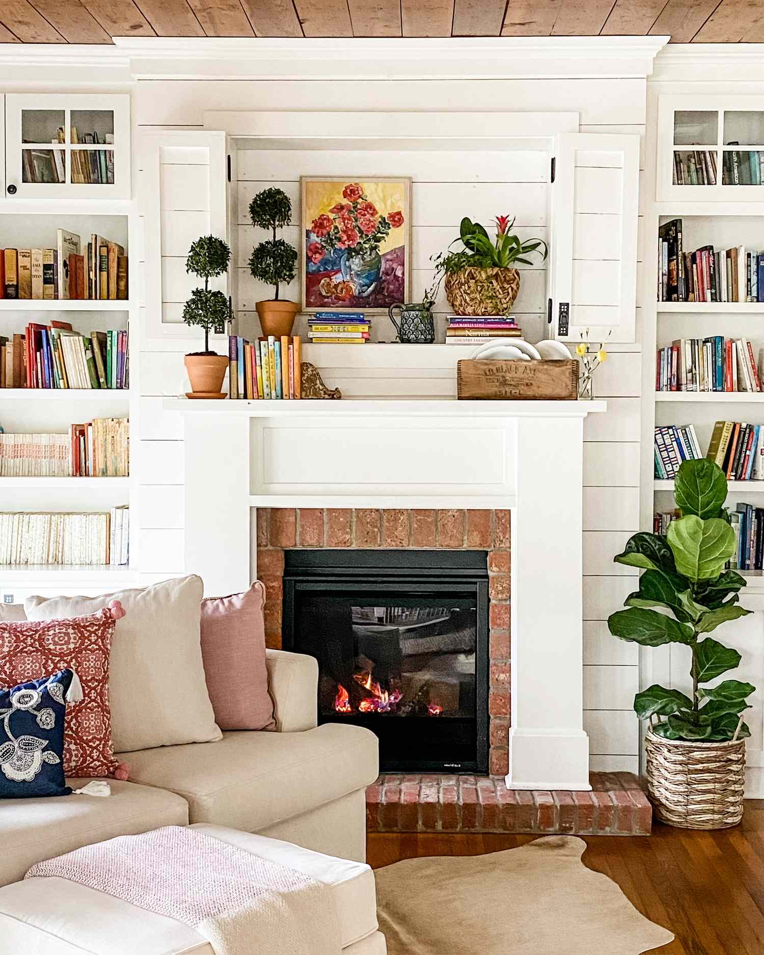 A mantel above a fireplace decorated with books plants and framed art in a cozy living room with bookshelves