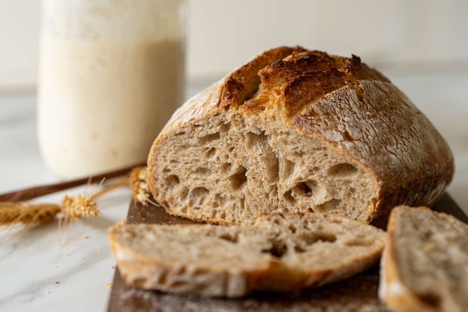 Loaf of rustic bread with slices and a jar in the background