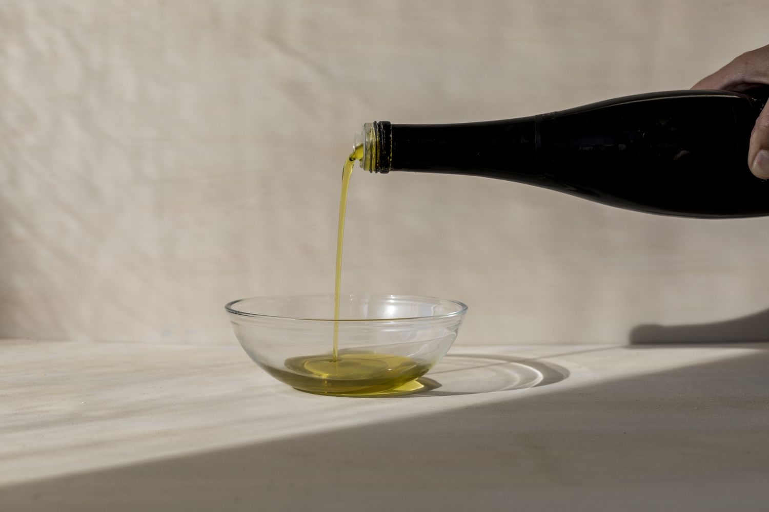 pouring olive oil from a darlk glass bottle into a glass bowl 