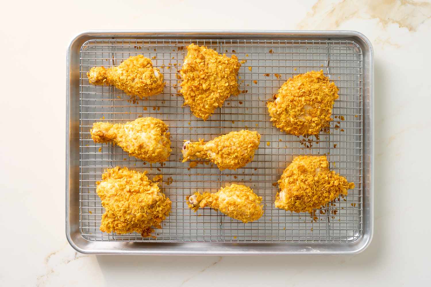 Eight pieces of baked chicken coated with crushed cornflakes on a cooling rack