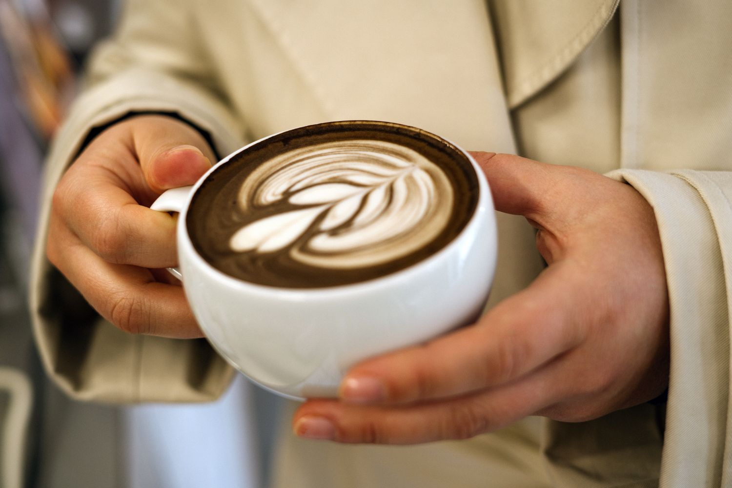 A person holding a cup of coffee with latte art on the surface