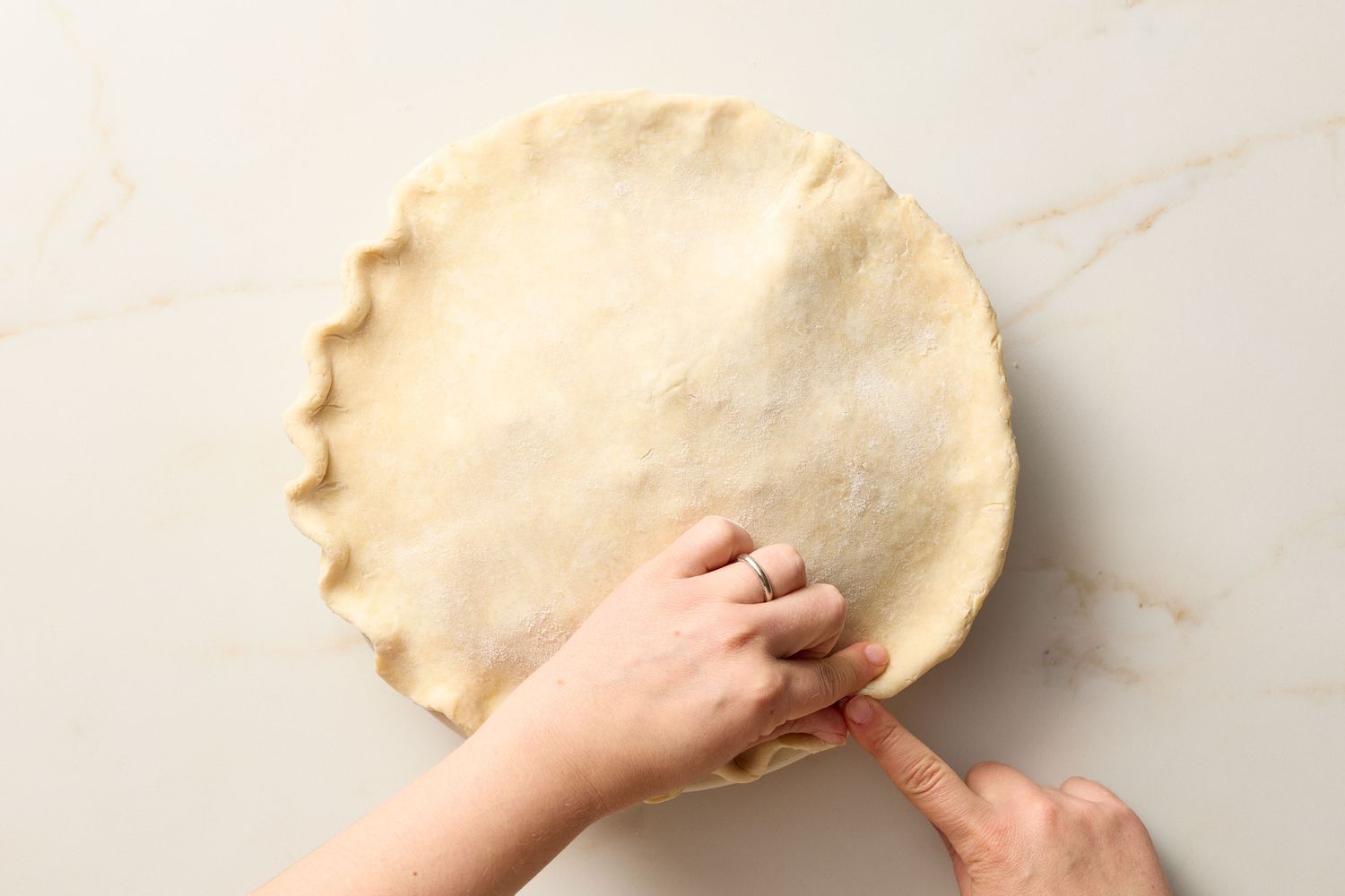Hands crimping the edges of a pie crust
