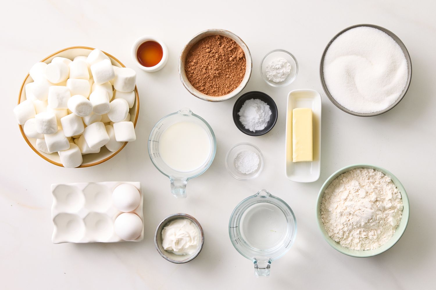 Marshmallows cocoa powder sugar flour butter milk and eggs arranged as ingredients for baking