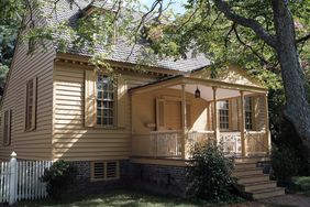 A traditional house with a wooden porch surrounded by greenery and a fenced yard