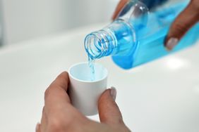 Woman pouring blue mouthwash into cup