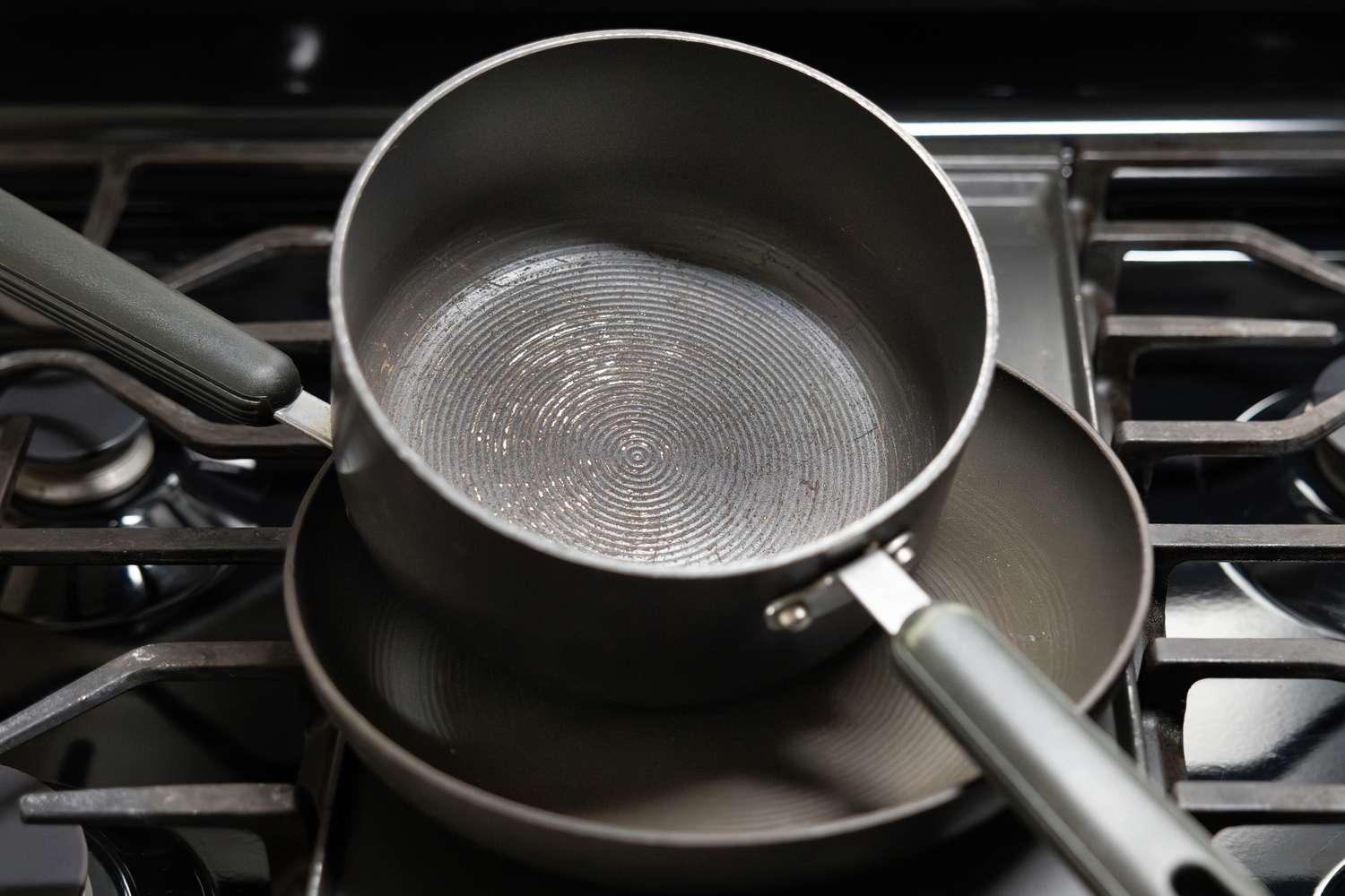 Two cooking pots one stacked inside the other sitting on a stovetop with visible scuffs and scratches on their surfaces