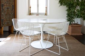 Round white table with wire chairs indoor setting with a carpeted floor and decorative backdrop