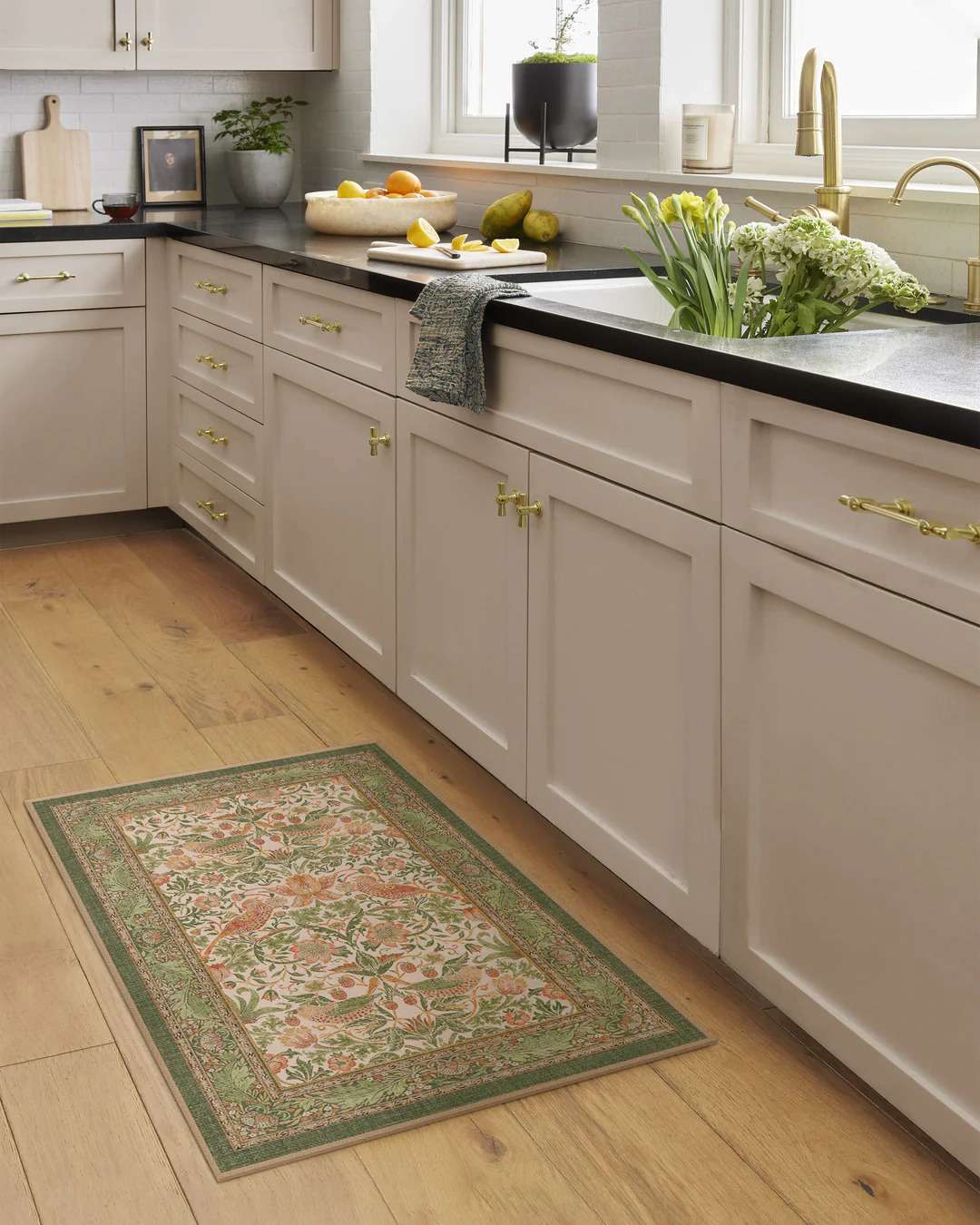 Morris & Co. strawberry thief sage rose rug in a white cabinet kitchen with black countertops. 
