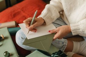 A person writes on a card placed on an envelope seated next to giftwrapping materials