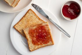 Toasted bread with strawberry jam on a plate next to a knife and a small bowl of strawberry jam