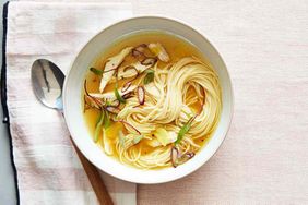 A bowl of noodle soup with garnish and a spoon placed on a cloth napkin