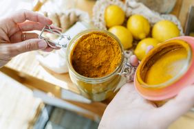 Hands opening a jar filled with turmeric and spices, lemons on a wooden countertop