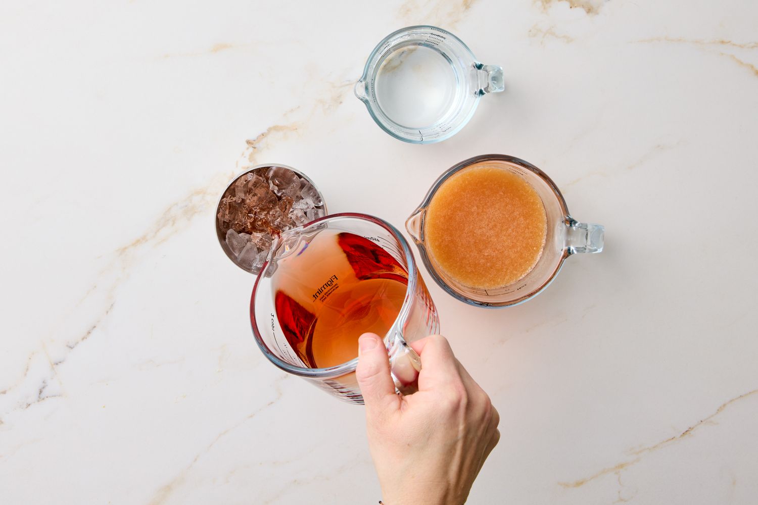 Ingredients for a cocktail including a glass pitcher with liquid and a persons hand preparing the drink