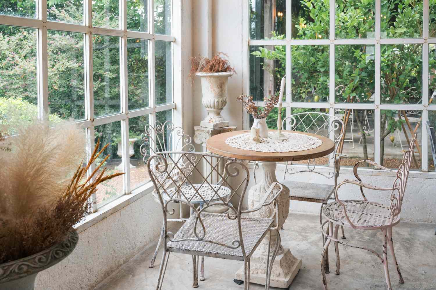 A small table set with chairs in a cozy room with large windows and greenery outside