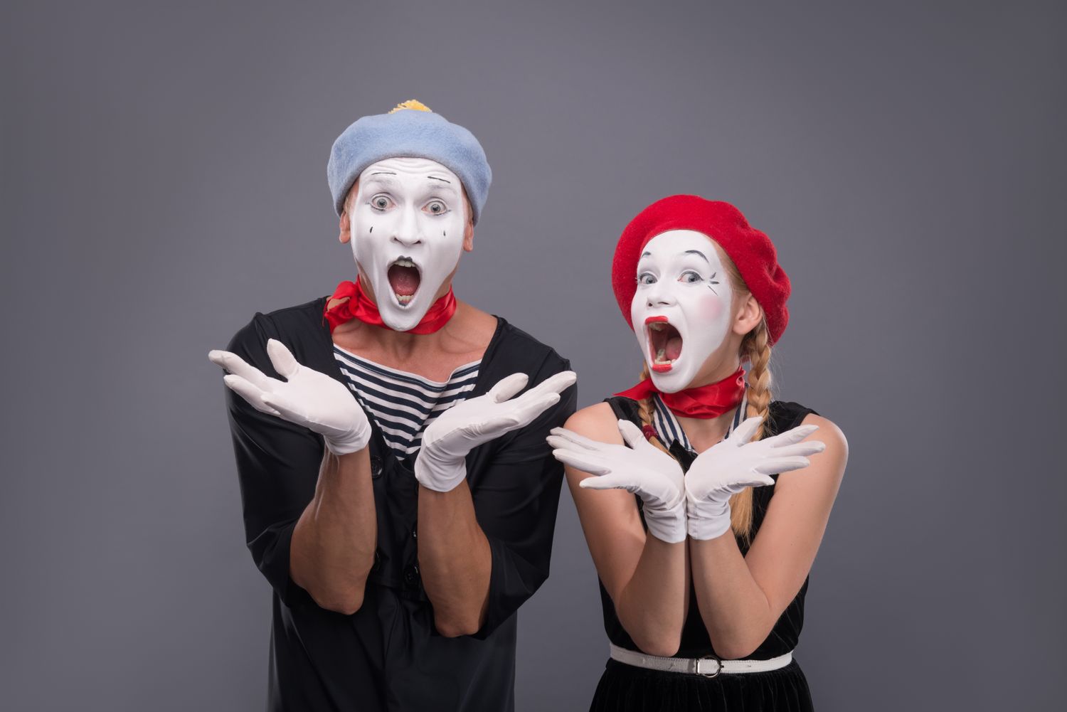 Two mimes with painted faces looking surprised performing expressive poses wearing berets and gloves