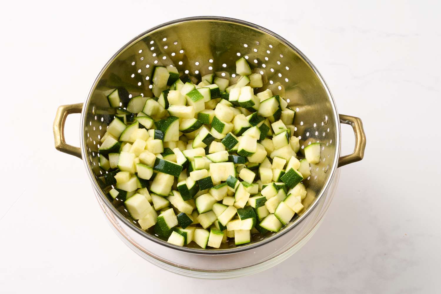 Diced zucchini draining in a metal colander on a countertop