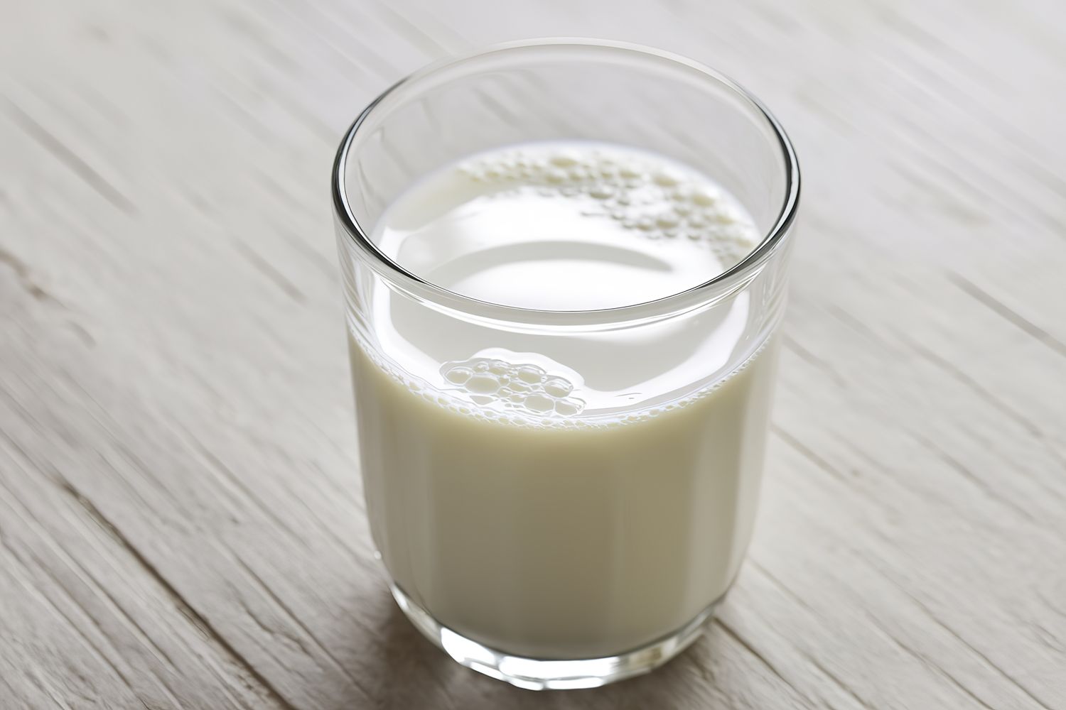 A glass filled with milk placed on a wooden surface