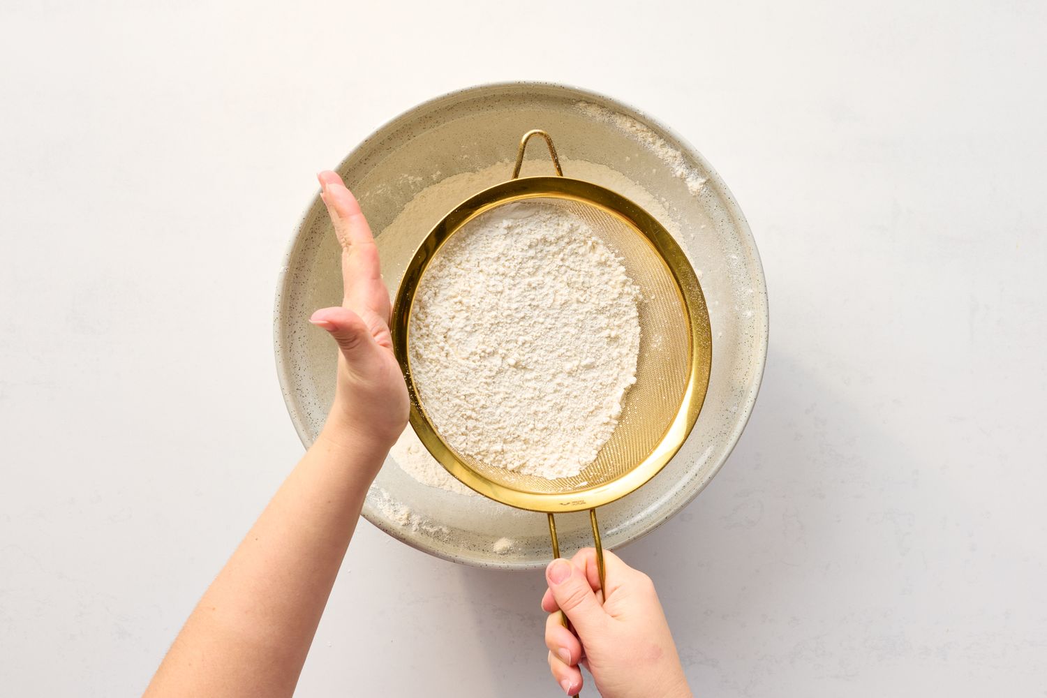 A person sifting flour into a bowl using a fine mesh sieve