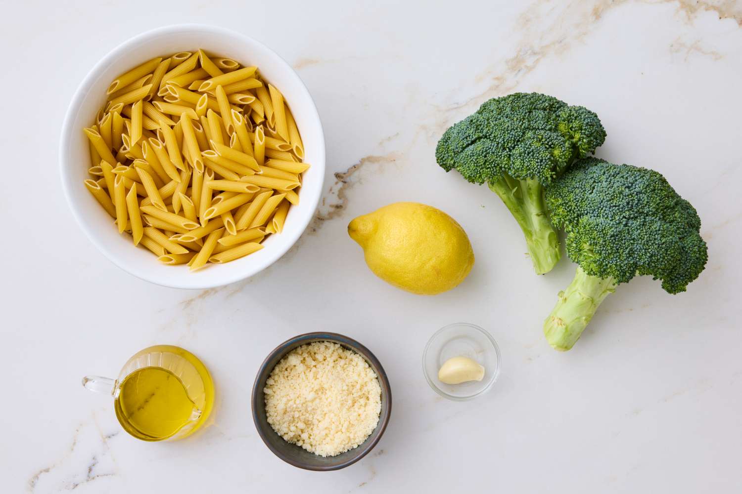 Ingredients for a pasta dish including penne broccoli lemon garlic Parmesan cheese and olive oil