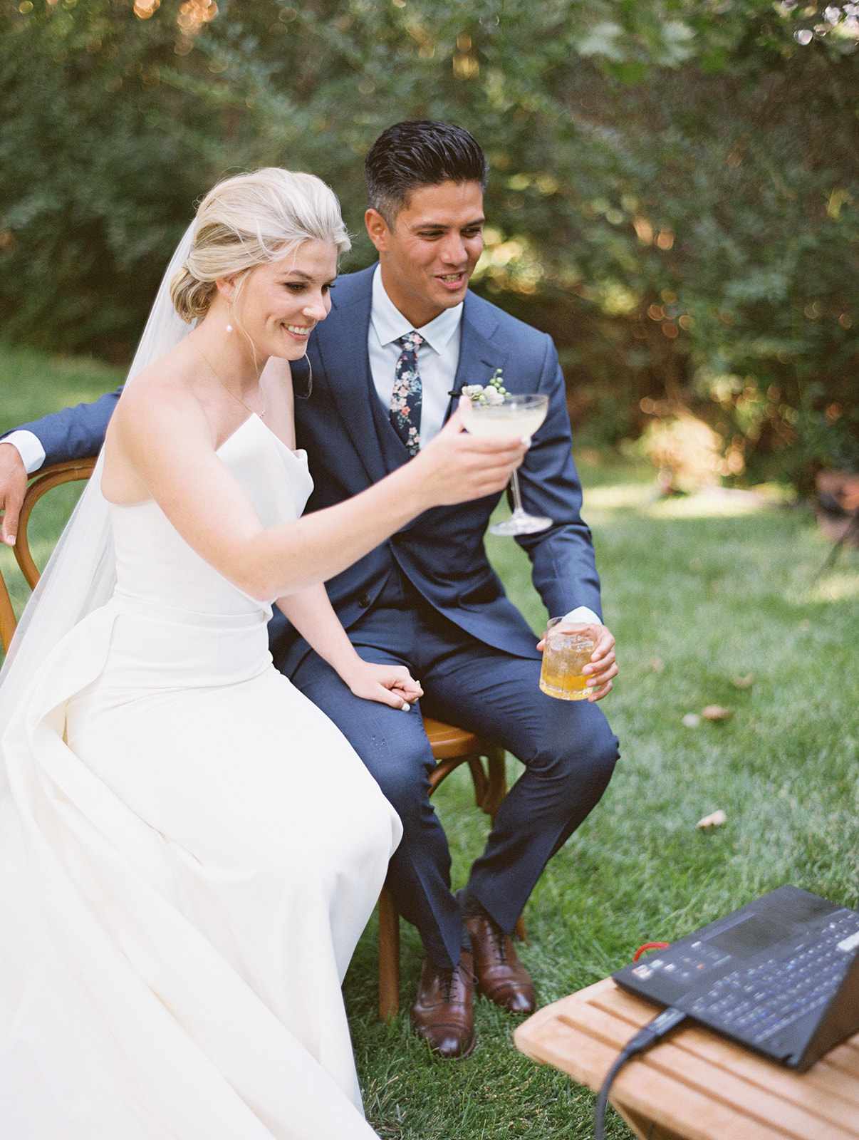 bride and groom holding cocktails during zoom call with virtual wedding guests