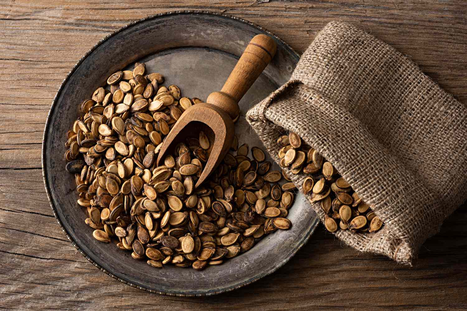 dried watermelon seeds in a metal try with wooden scoop