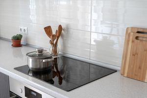 A modern kitchen countertop with a pot on an induction cooktop wooden utensils in a holder a cutting board and a small potted plant