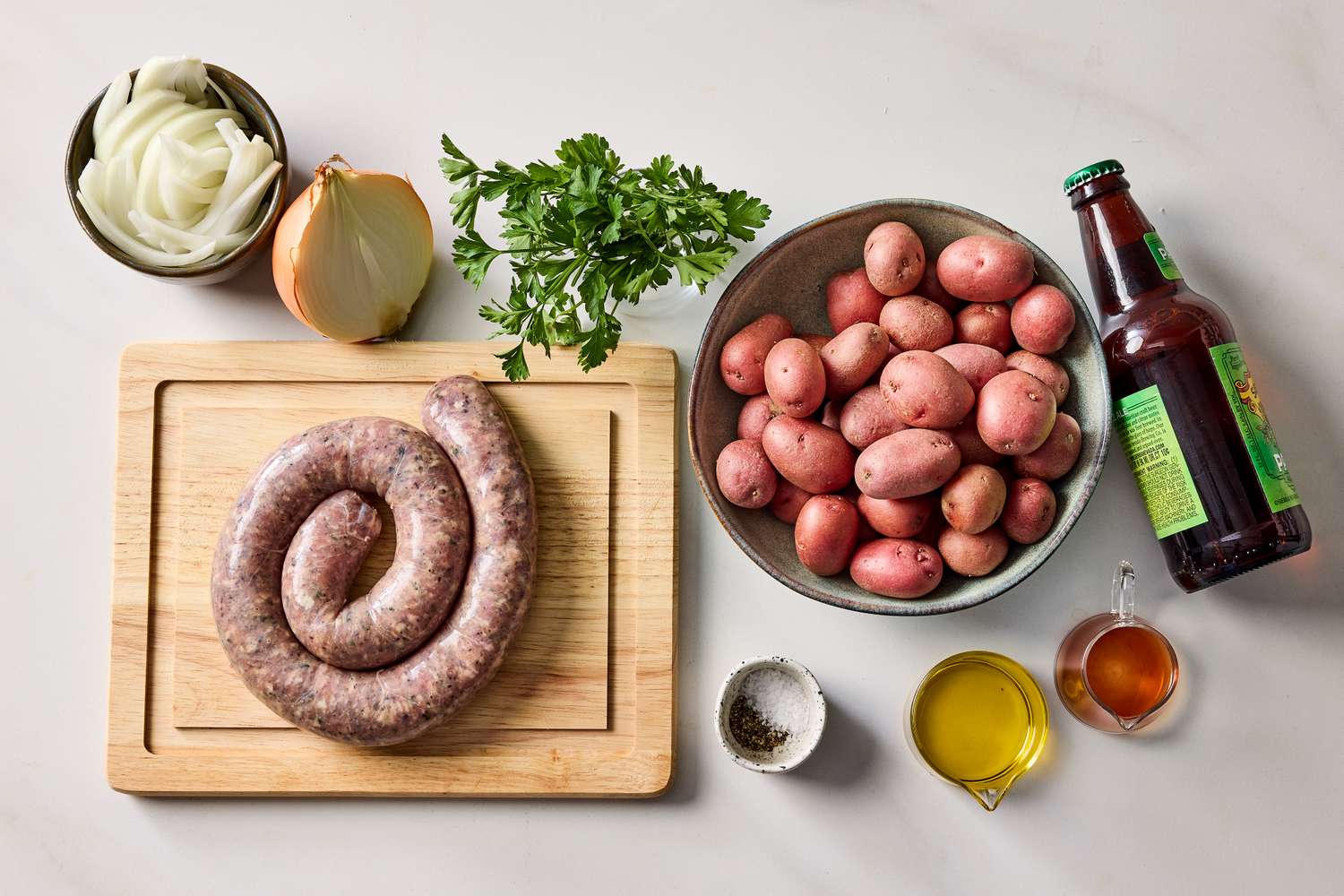 Ingredients for beerbraised sausages with warm potatoes including sausages potatoes onion parsley beer oil and seasonings
