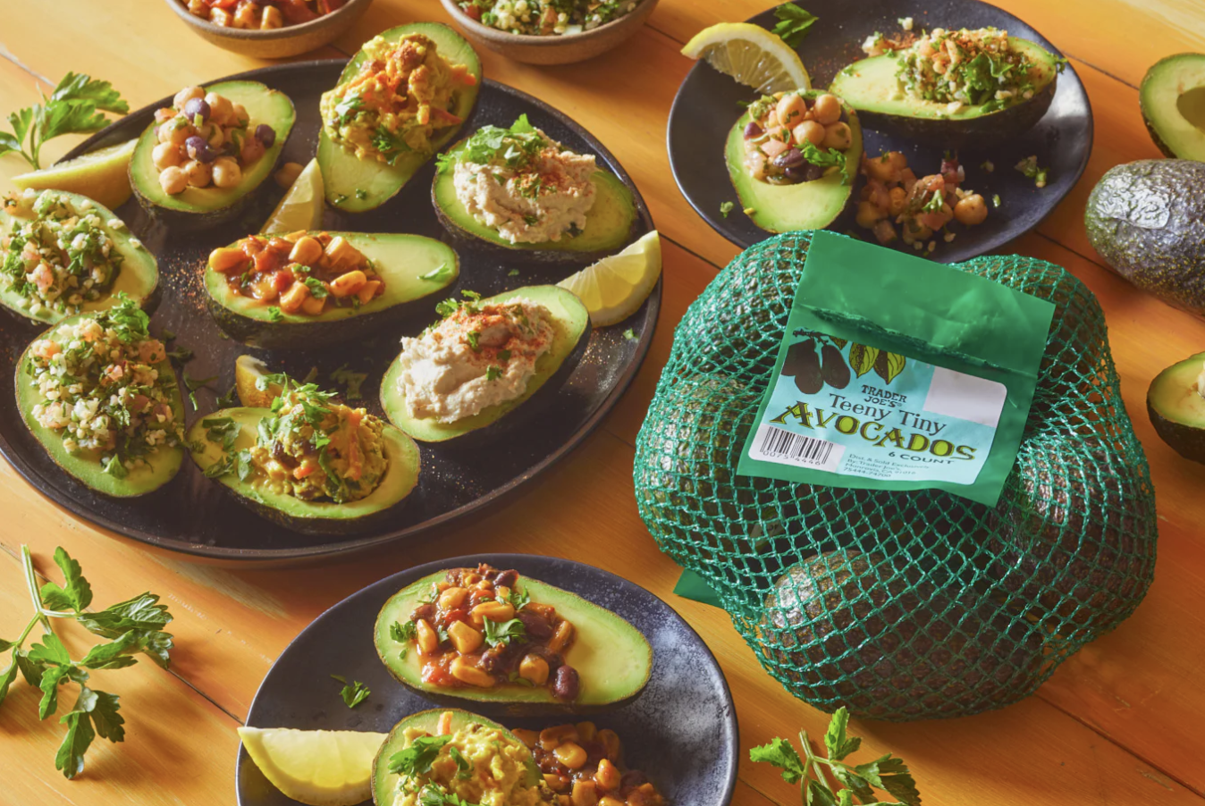 Halved avocados filled with various toppings on plates with a netted bag of Trader Joes avocados in the scene