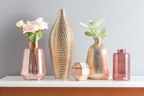 A set of decorative vases and containers some with flowers or greenery arranged on a white shelf