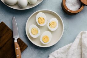 A plate containing four halved hardboiled eggs a knife and cloth napkin nearby