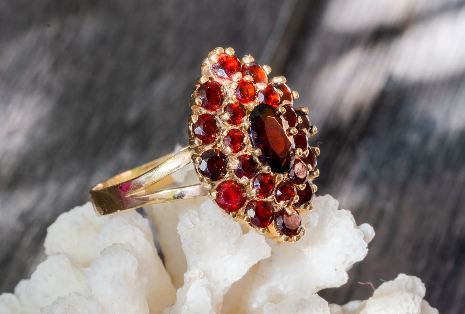 A gold ring adorned with multiple garnet stones resting on a coral piece against a dark wood background