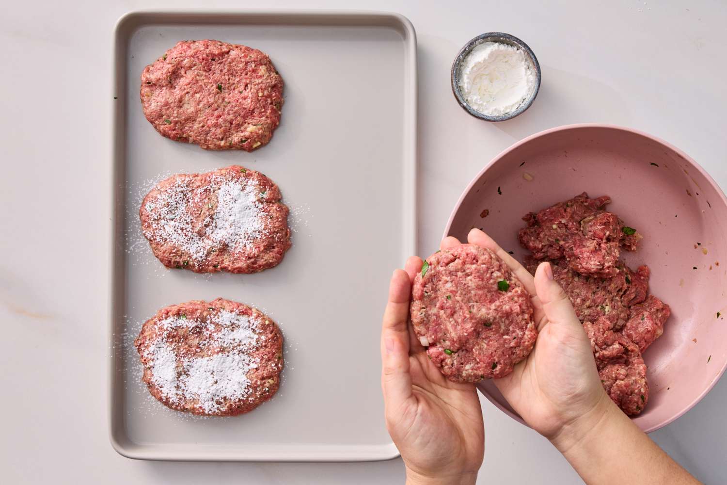 Shaping a patty with seasoned ground meat mixture on a tray and in a bowl